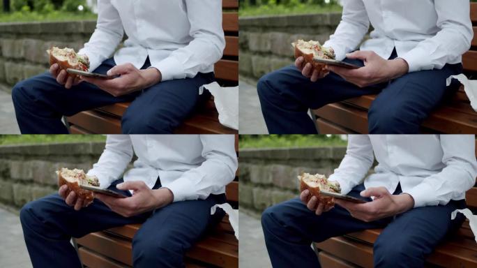 坐在街头长凳上的男子在智能手机上打字并拿着汉堡