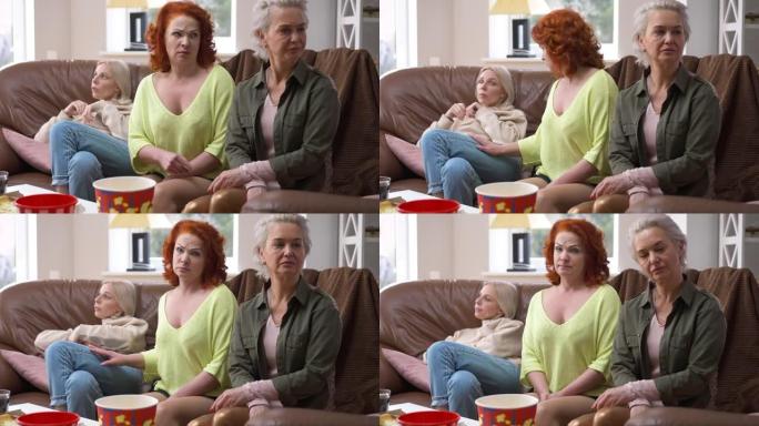 红发成年女性的肖像与坐在客厅触摸肩膀的朋友争论，看着相机摇头。在室内与得罪的朋友在一起使白人女士心烦