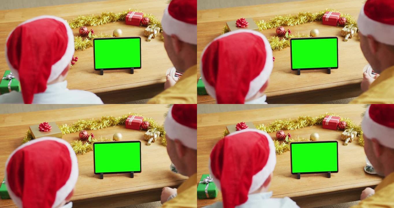 戴着圣诞老人帽子的高加索父子制作平板电脑圣诞视频通话，绿屏
