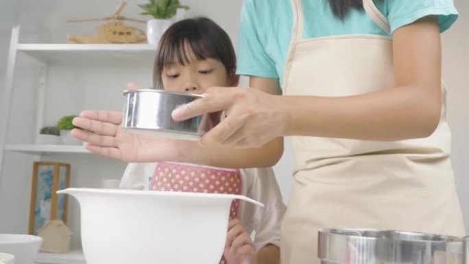 快乐的亚洲孩子在家学习制作饼干，女孩将面粉筛入搅拌碗。