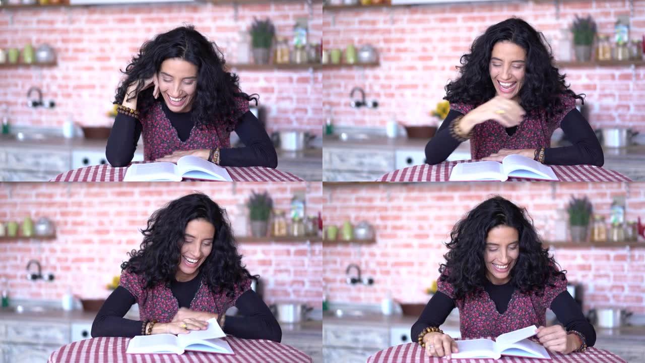 4k视频笑着卷曲的黑发女人坐在厨房的桌子上，在家看书
