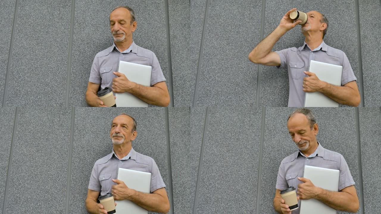 年长同事的男性肖像，带着银色的笔记本电脑和一杯咖啡，早上在深灰色的墙壁附近等待会议，远程工作，喝咖啡