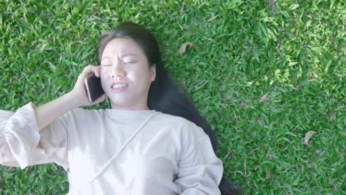 东南亚女子拿着手机躺在绿草上