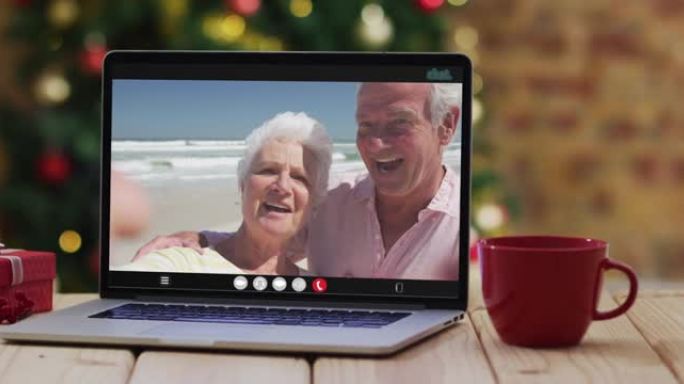 一对白人老夫妇在圣诞树旁用笔记本电脑视频通话