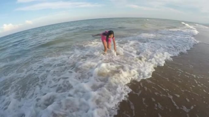 穿着粉红色泳衣的快乐亚洲女孩和她的兄弟在度假期间一起在海滩上享受海浪。