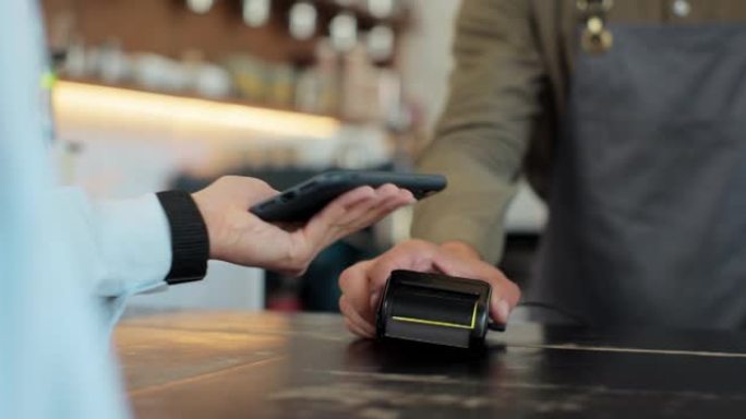 一名女子手持智能手机，该智能手机采用NFC支付技术，用于在咖啡馆内支付外卖咖啡。客户使用移动设备通过