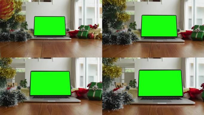 笔记本电脑上有绿屏复制空间，桌子上有圣诞老人帽子、圣诞树和礼物