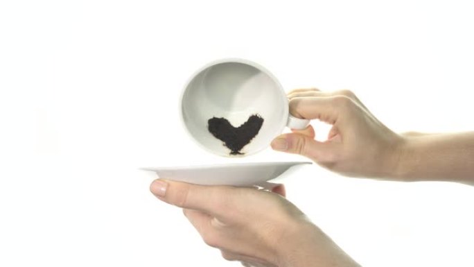 女性的手翻过一个白色的杯子，里面的咖啡渣呈心形。特写