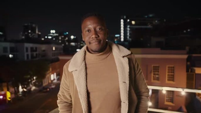 黑人男性站在城市的屋顶上，在夜晚欢快地微笑。高质量4k镜头