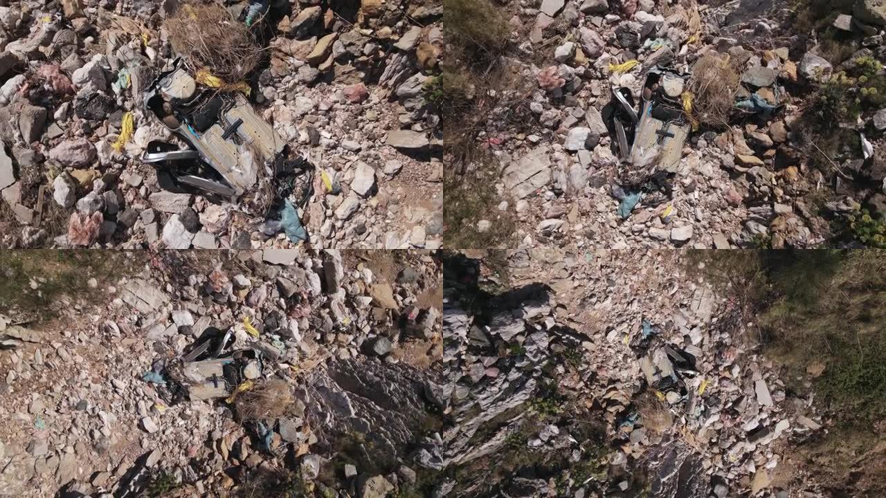 完全破碎的生锈汽车残骸躺在岩石，碎片和干燥的树枝之间，带有摄像头的无人机绕轴缓慢上升。由于事故，被毁