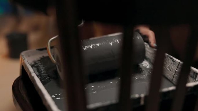 椅子的特写镜头，上面放着一个托盘，一个装有灰色油漆的容器，一个拿着大滚筒的女人的手在平滑的运动中获得