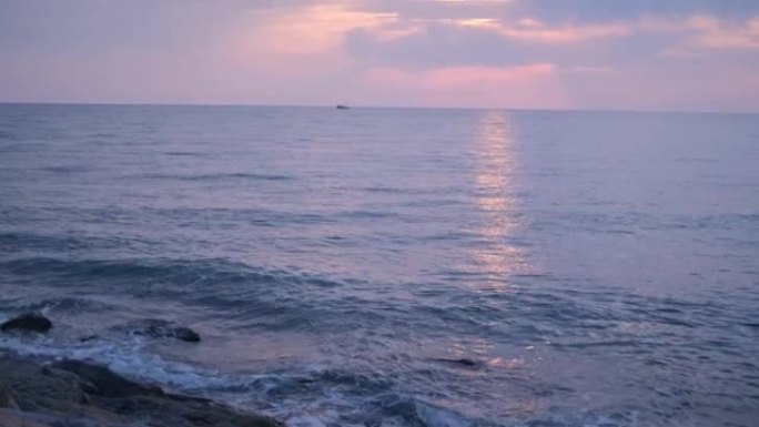 海浪在海上轻拂。有岩石的海岸 .. 鹅卵石很小。日落。地平线。