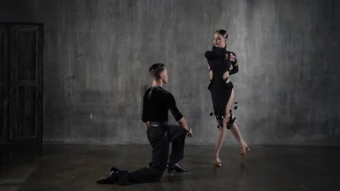年轻优雅的千禧一代舞蹈舞厅夫妇穿着黑色连衣裙，在垃圾背景下以性感的姿势跳舞。