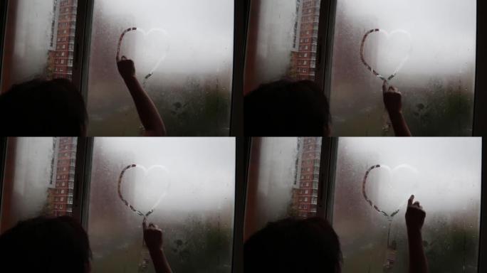 一个女孩用手指在雾蒙蒙的窗户上画一颗心。爱情和浪漫的概念