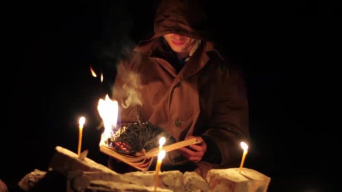 一个穿着斗篷的男人正在读一本热书，地上放着蜡烛