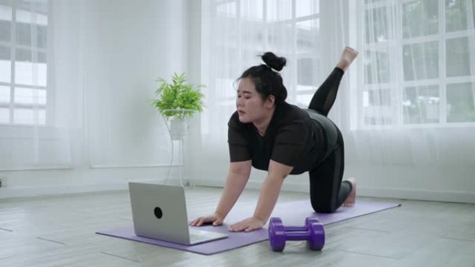 胖女人通过跟踪笔记本电脑上的视频片段来锻炼身体，以在家中客厅减肥。