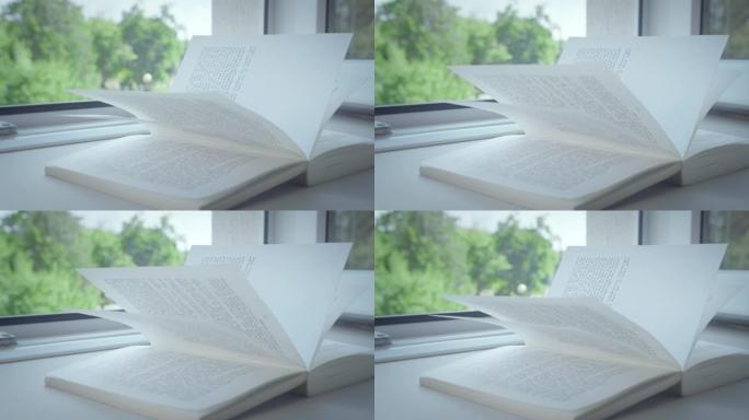 一本书躺在敞开的窗户的窗台上，书页上的阳光，特写