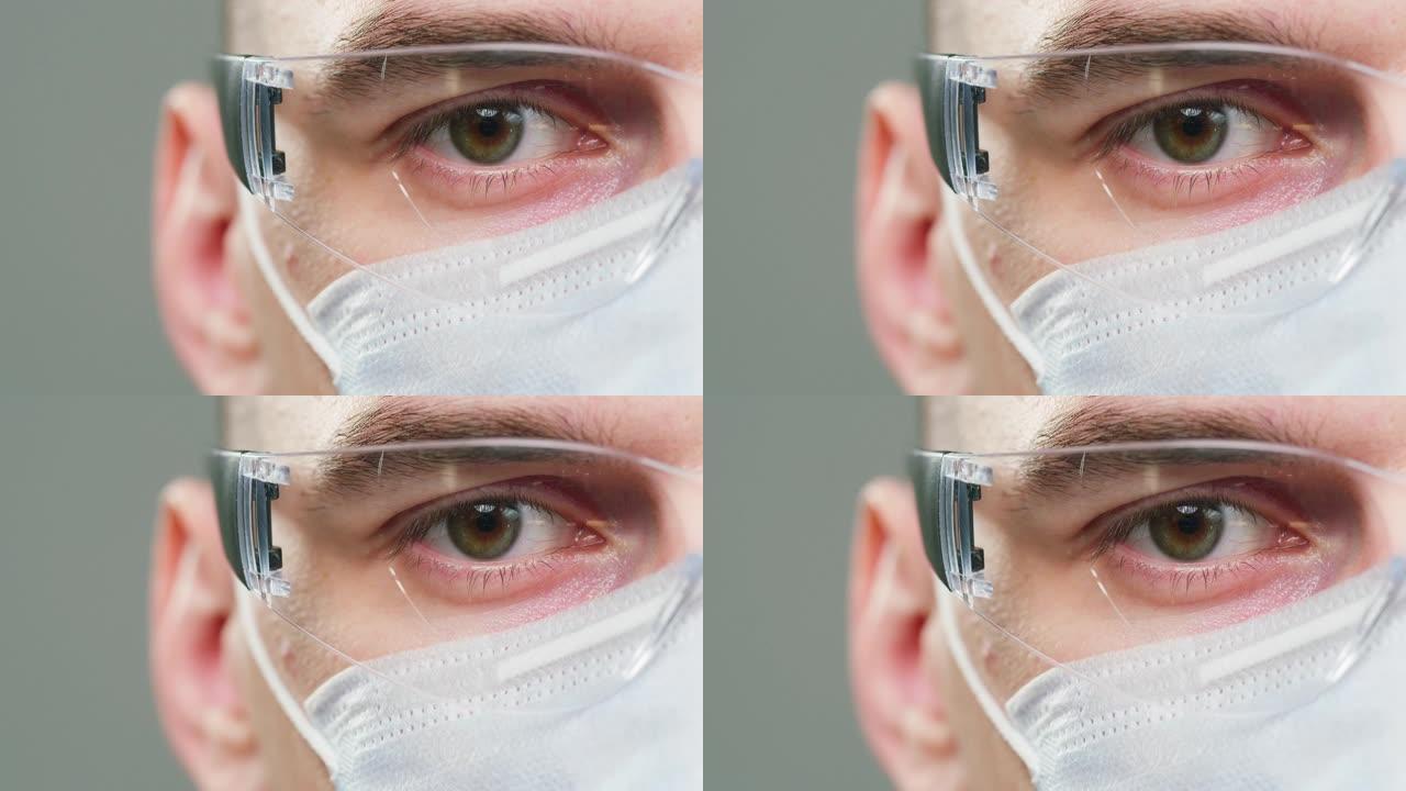 医生的特写，科学家专家戴着医用防护眼镜和口罩，在相机中穿着制服的男性专业化学家的半脸肖像，孤立在灰色