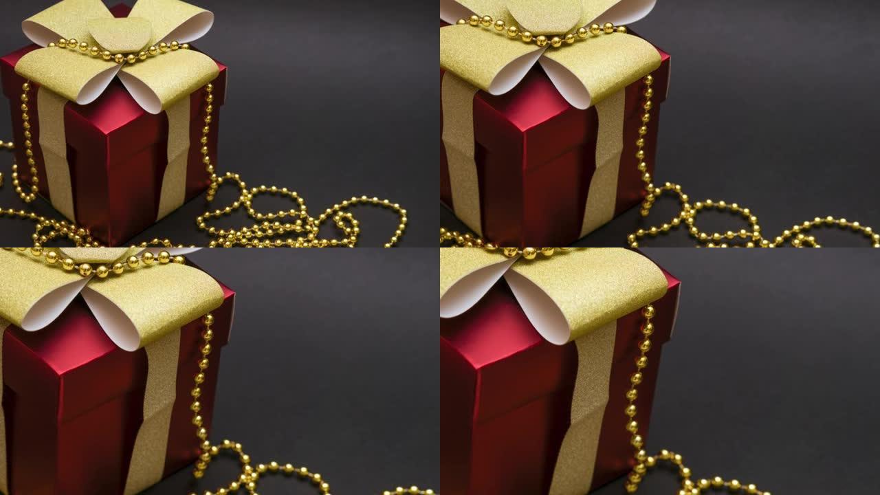 黑色背景上带有金丝带和金色珠子的红色礼品盒。