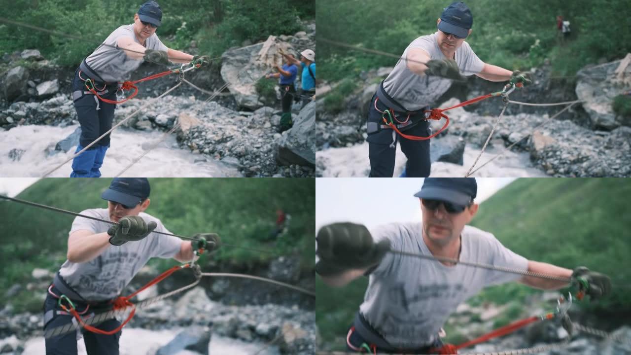 一个人在徒步旅行中穿过一条快速的山河。一名游客使用垂直绳索过河，并用登山扣固定