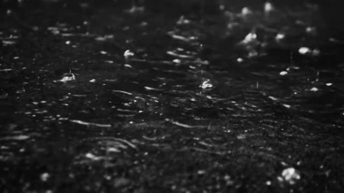 黑暗中的雨。飞溅的水落在地上。街上倾盆大雨。雨滴落在沥青上，美丽的雨中黑白分明。雨背景