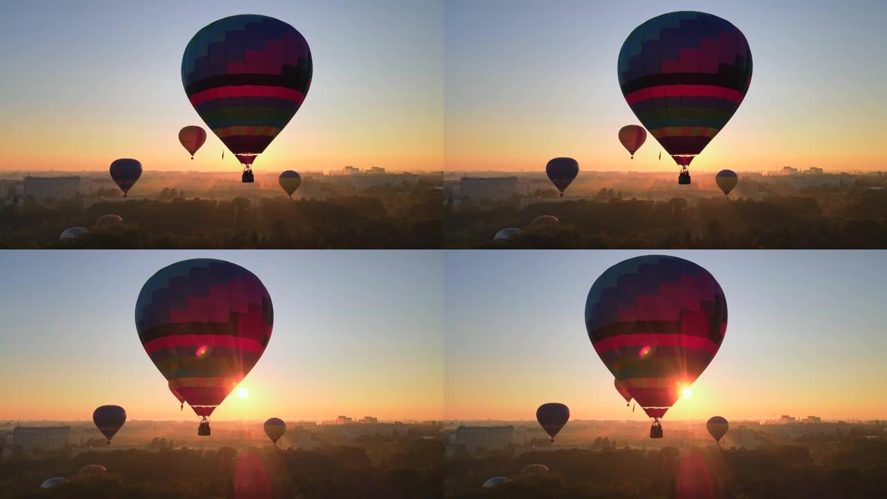 夏季日出时，彩色热气球在欧洲小城市绿色公园上空飞行的空中无人机视图剪影。HDR视频