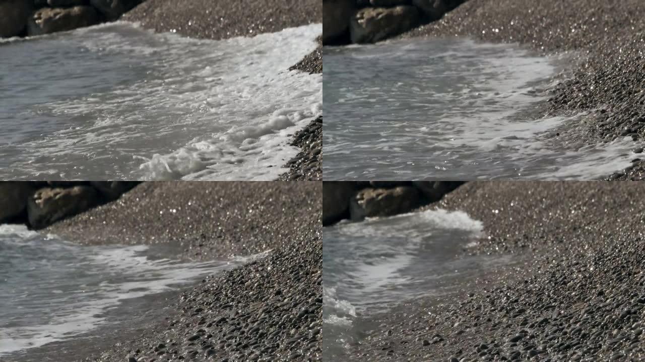 圆石滩上波浪滚滚的特写镜头。前景中有小卵石。欧洲中部海岸温暖而柔和的海浪。卵石滩的海水膨胀。
