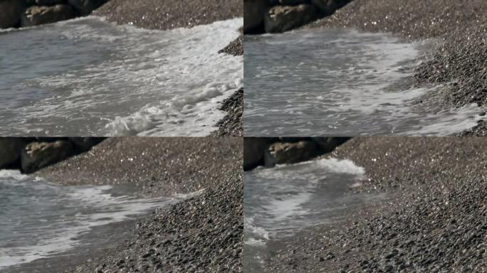 圆石滩上波浪滚滚的特写镜头。前景中有小卵石。欧洲中部海岸温暖而柔和的海浪。卵石滩的海水膨胀。
