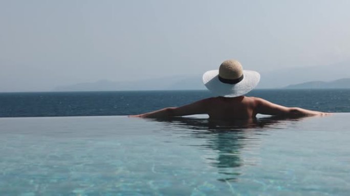 戴着草帽的女人在无边游泳池放松，在豪华度假村享受海景