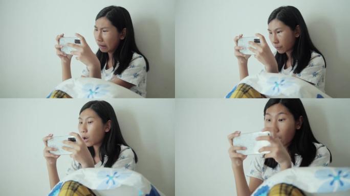 亚洲女孩在家坐在床上玩手机游戏，生活方式概念。