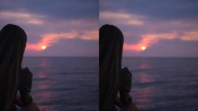 女孩垂直视频的剪影。海浪在海上轻拂。有岩石的海岸 .. 鹅卵石很小。日落。地平线。