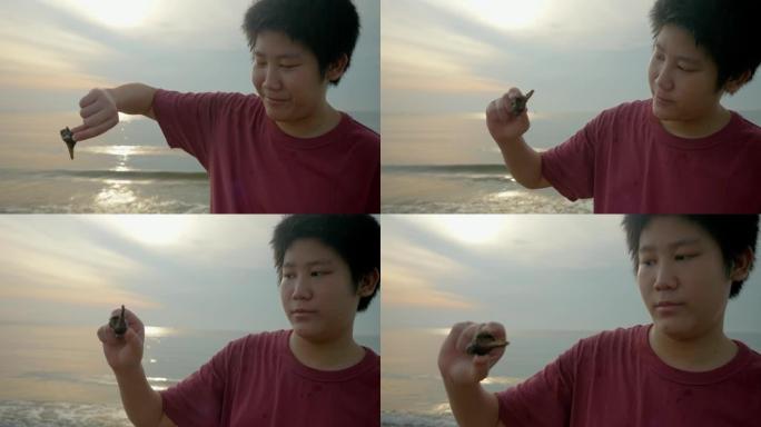 亚洲男孩在海滩上用日出捕捉寄居蟹，生活方式概念。