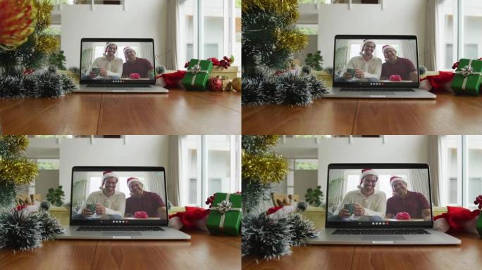 微笑的混血儿父子戴着圣诞老人的帽子在笔记本电脑上的圣诞节视频通话中
