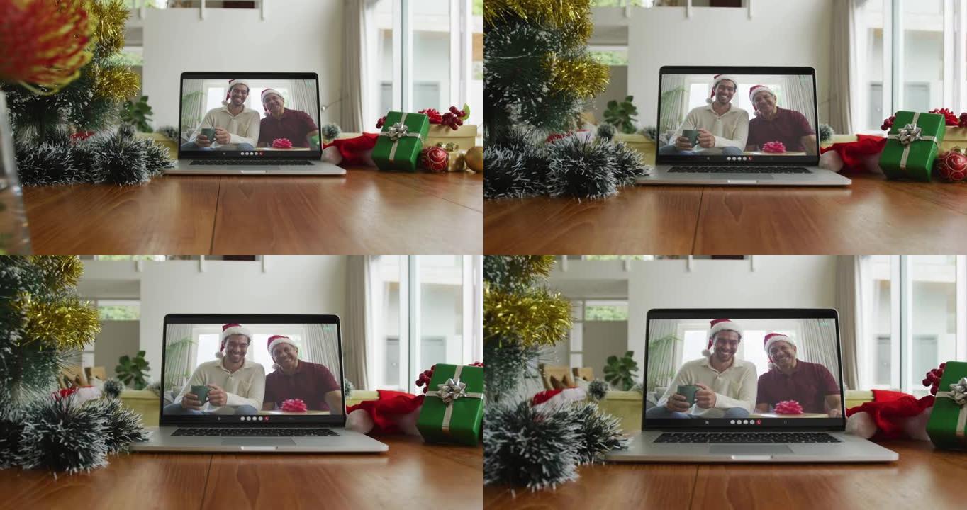 微笑的混血儿父子戴着圣诞老人的帽子在笔记本电脑上的圣诞节视频通话中