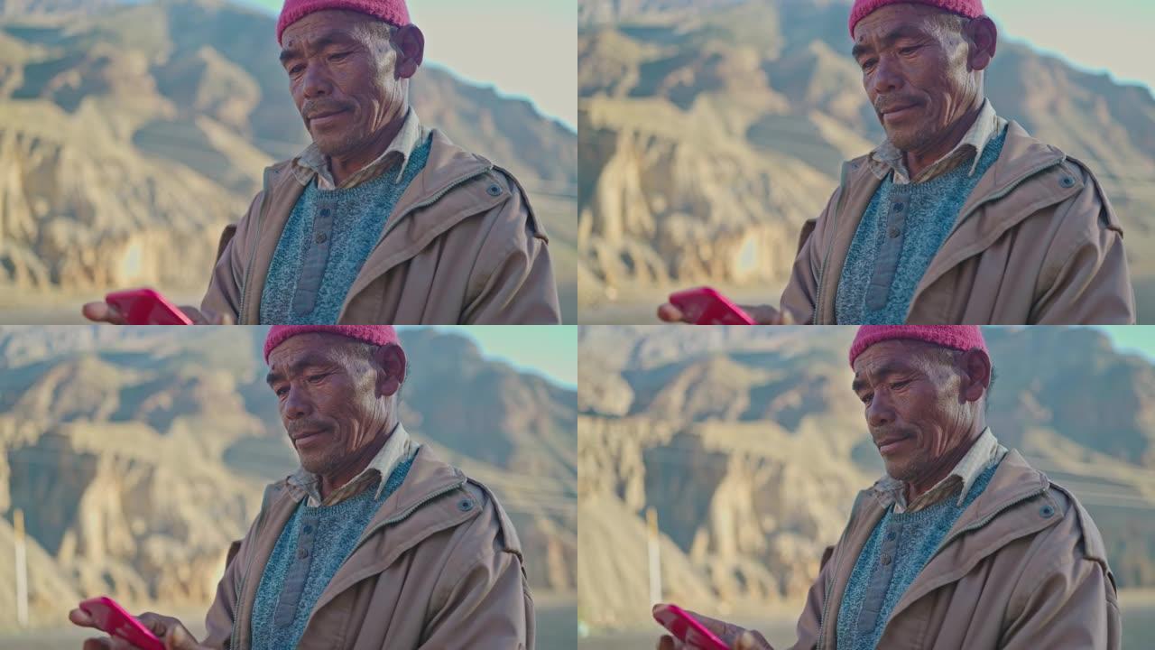 东亚老人站在贫瘠的土地上使用智能手机