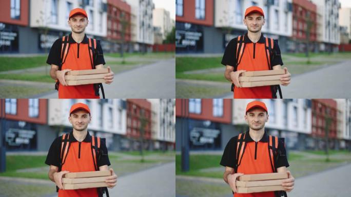 年轻的快递送货员的肖像，红色的背包在纸箱中拿着披萨，在居民区等待顾客。送货服务。出色的交付
