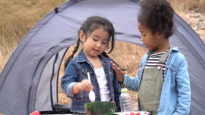 一群不同的非裔美国人和亚裔女孩在乡村自然公园露营地的帐篷外一起吃西瓜和水果