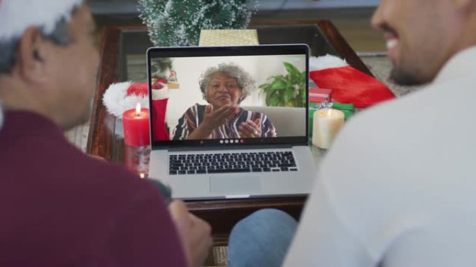 微笑的混血儿父子使用笔记本电脑与屏幕上的高级女性进行圣诞节视频通话