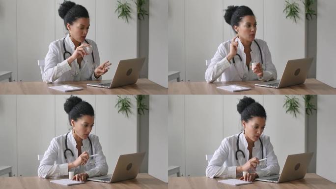 一位年轻的女医生使用笔记本电脑与患者进行在线视频咨询。美国黑人妇女坐在医院办公室的桌子旁。特写。慢动
