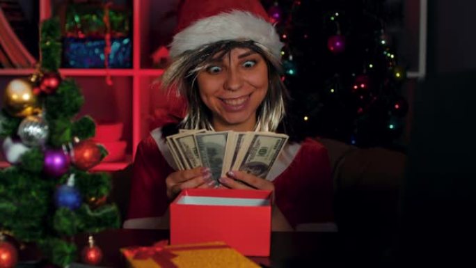 一个穿着圣诞老人服装的年轻女子坐在办公室电脑前的椅子上数钱。穿着新年西装和帽子的女商人经理，在工作场