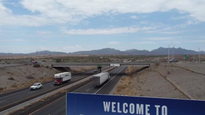 4k无人机倾斜悬臂拍摄来自加州10号州际公路高速公路的亚利桑那州欢迎标志，卡车汽车和蓝色多云的天空