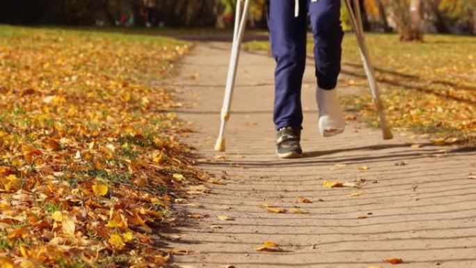 孩子拄着拐杖在秋季公园散步。女孩的一条腿骨折了。