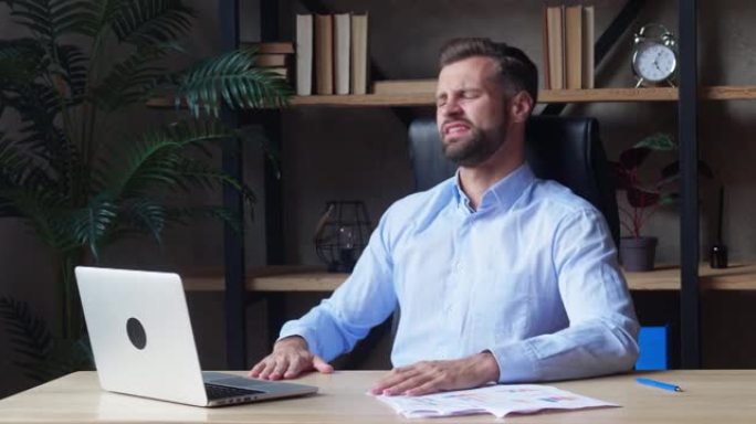 一位穿着蓝色衬衫的商人专心致志地看着笔记本电脑屏幕，并表达出一种烦恼的情绪。公司失败或交易不成功