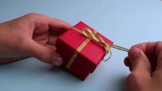双手解开红色礼品盒上的金丝带。