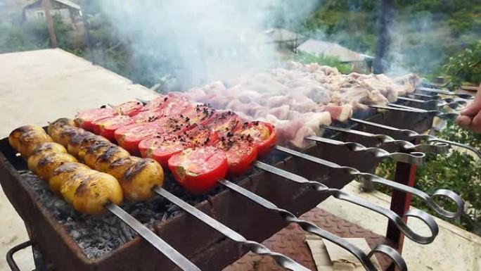 厨师在村子里准备烧烤。猪肉着火了。火上的红色西红柿、黄色短裤和猪肉。厨师的飞行菜