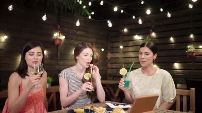 迷人而快乐的一群高加索女性朋友，一边享受鸡尾酒，一边通过视频通话与朋友保持联系