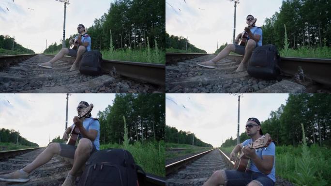 戴着墨镜和帽子的男人坐在铁路铁轨上弹吉他