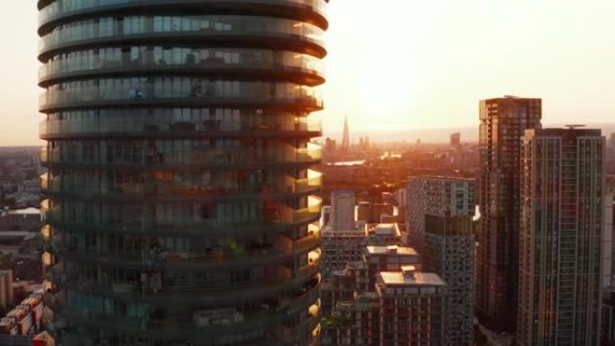 飞抵金丝雀码头区高大的现代圆柱形住宅建筑竞技场塔。日落时间的未来派城区。英国伦敦