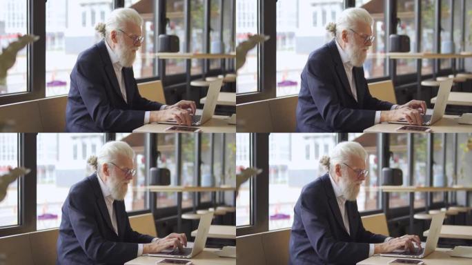 现代老年男性在笔记本电脑上编辑文本，在咖啡馆工作，在线教育