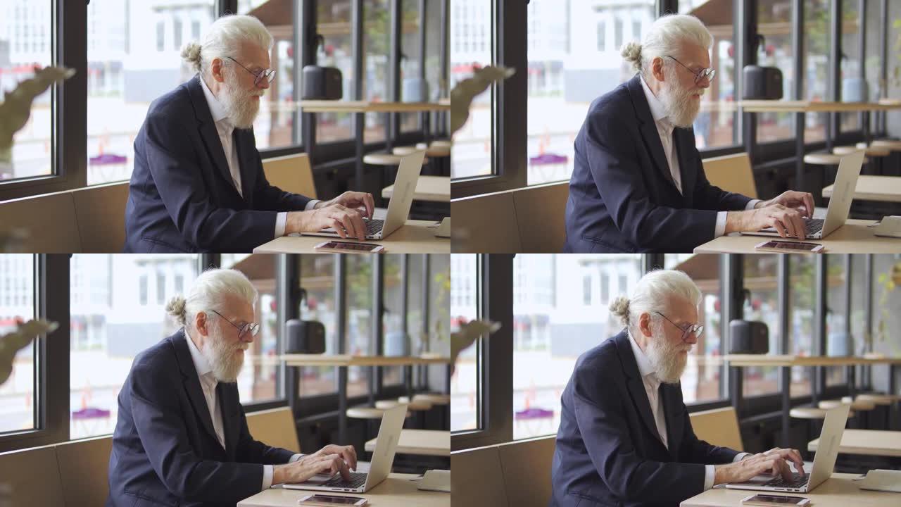 现代老年男性在笔记本电脑上编辑文本，在咖啡馆工作，在线教育